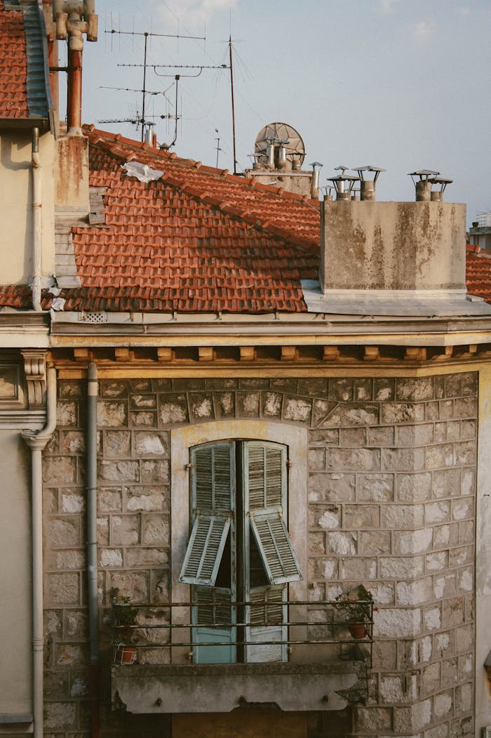 Exterior view of a charming historic stone house with open shutters and a small balcony under a clear sky.